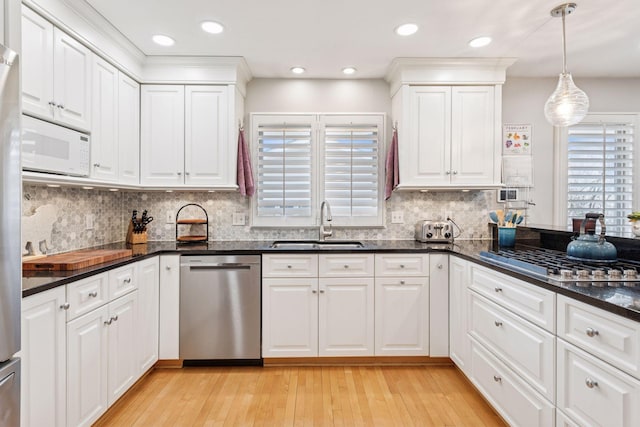 kitchen featuring appliances with stainless steel finishes, a sink, light wood-type flooring, white cabinetry, and backsplash