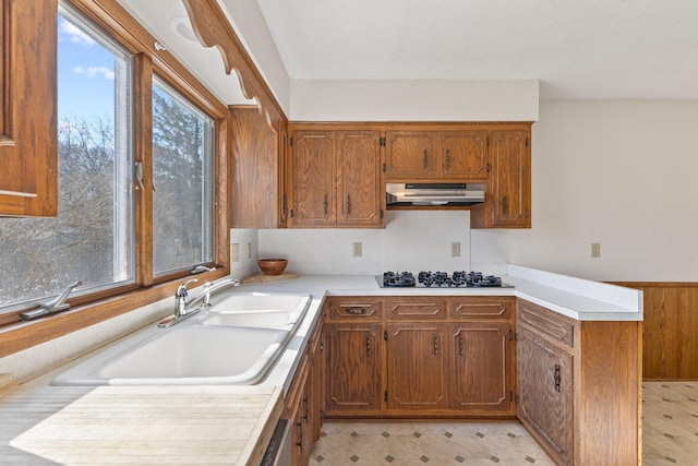 kitchen with under cabinet range hood, a sink, brown cabinetry, light countertops, and light floors