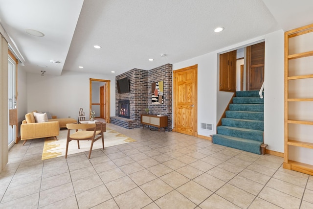 living area with visible vents, a textured ceiling, a fireplace, light tile patterned floors, and stairs