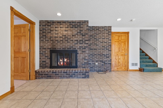 unfurnished living room featuring tile patterned floors, visible vents, a textured ceiling, stairway, and a fireplace