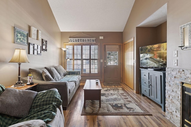 living room with dark wood-style floors, lofted ceiling, a stone fireplace, and a textured ceiling