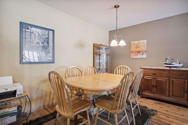 dining area with an inviting chandelier, light wood-style flooring, baseboards, and a textured ceiling