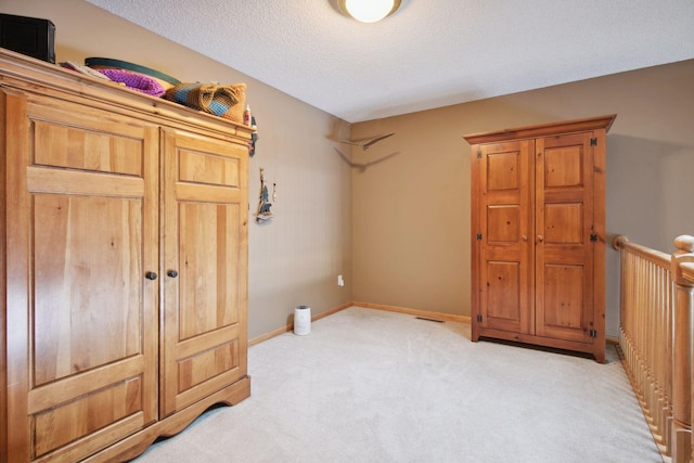 bedroom featuring light carpet, a textured ceiling, visible vents, and baseboards