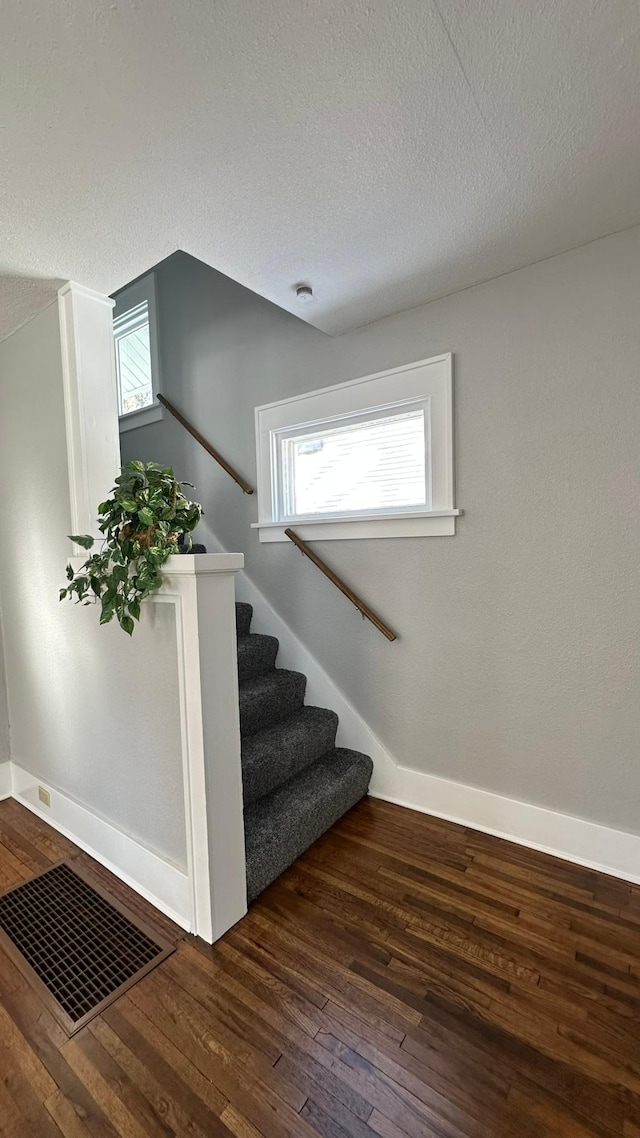 staircase featuring baseboards, a textured ceiling, visible vents, and wood finished floors