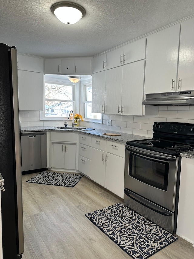 kitchen featuring light stone counters, appliances with stainless steel finishes, white cabinets, a sink, and under cabinet range hood