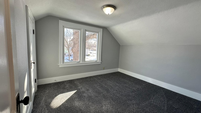 additional living space with a textured ceiling, vaulted ceiling, dark carpet, and baseboards