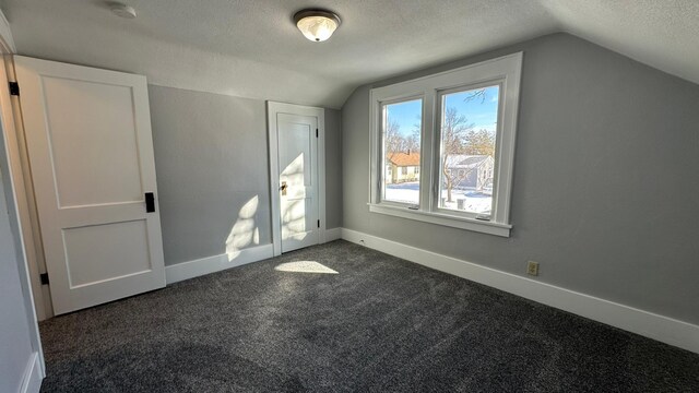 additional living space featuring a textured ceiling, dark colored carpet, vaulted ceiling, and baseboards