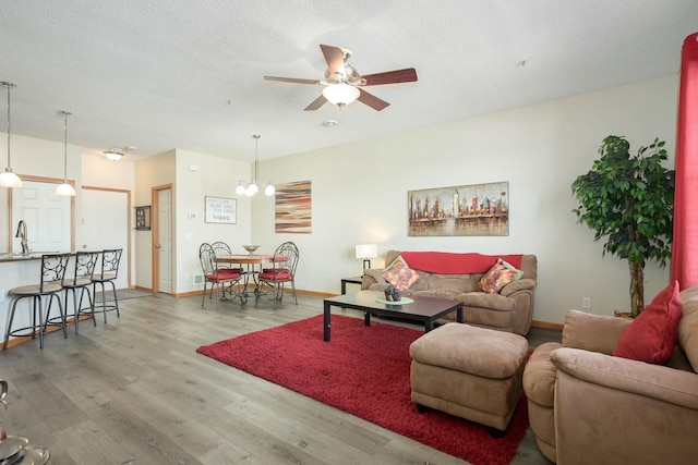 living area featuring a textured ceiling, baseboards, wood finished floors, and ceiling fan with notable chandelier