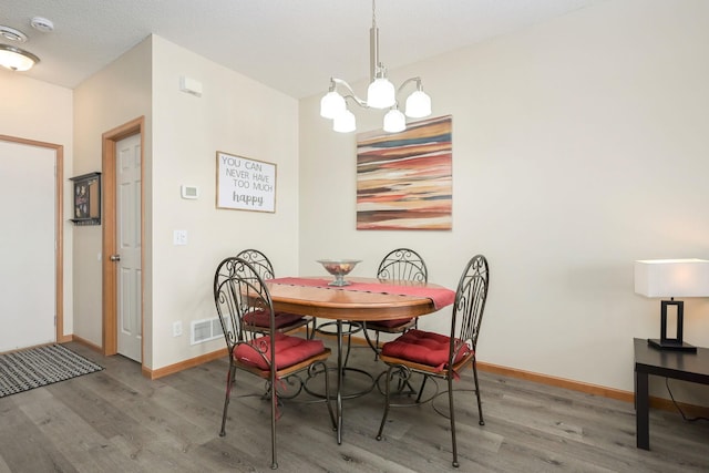 dining space featuring visible vents, baseboards, a chandelier, and wood finished floors