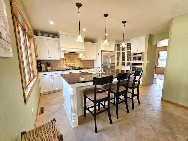 kitchen with visible vents, tasteful backsplash, stainless steel appliances, arched walkways, and white cabinets