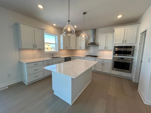 kitchen with wall chimney range hood, a kitchen island, visible vents, and white cabinets