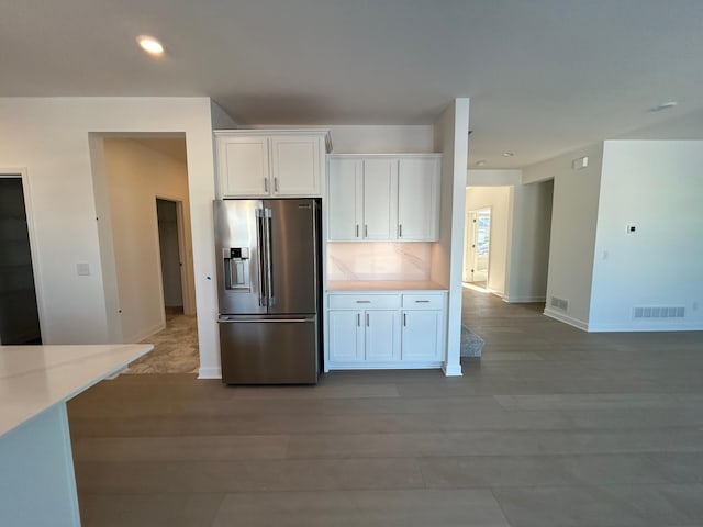 kitchen with visible vents, light wood-style flooring, white cabinetry, stainless steel refrigerator with ice dispenser, and backsplash