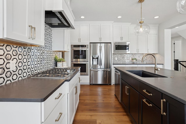 kitchen with decorative light fixtures, dark countertops, appliances with stainless steel finishes, white cabinetry, and a sink