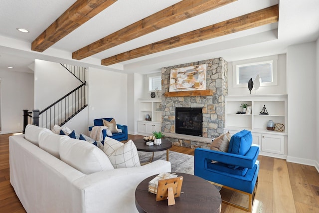 living area featuring light wood-style flooring, stairway, beamed ceiling, built in shelves, and a fireplace