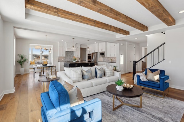 living area featuring light wood finished floors, baseboards, beamed ceiling, stairs, and a chandelier