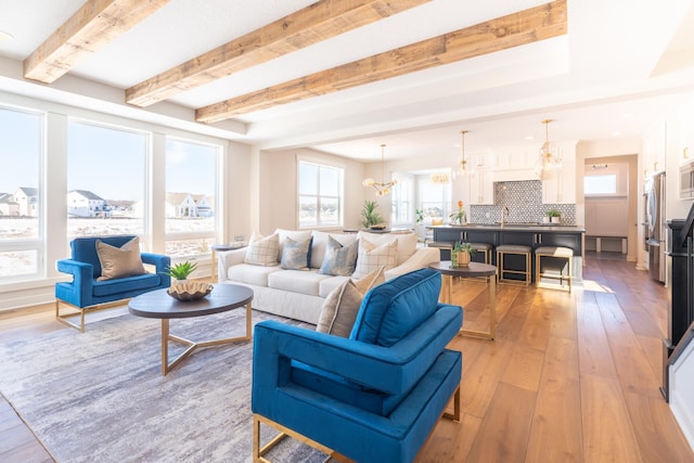 living area with light wood finished floors, a chandelier, and beamed ceiling