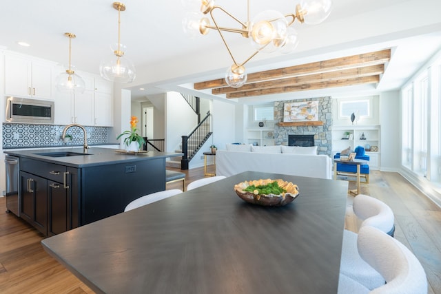 dining room featuring recessed lighting, stairway, light wood-style flooring, a stone fireplace, and beamed ceiling