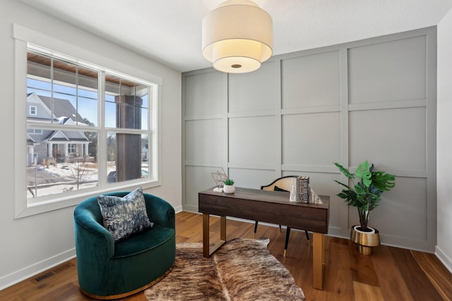 office featuring baseboards, wood finished floors, visible vents, and a decorative wall