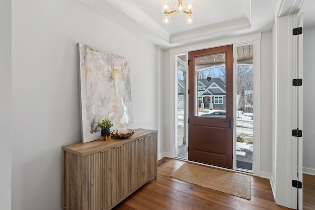 entrance foyer with an inviting chandelier, baseboards, a raised ceiling, and dark wood finished floors