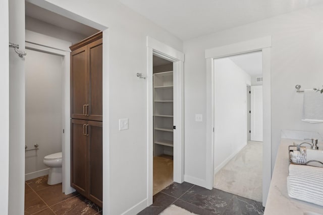 bathroom featuring a walk in closet, baseboards, visible vents, and toilet