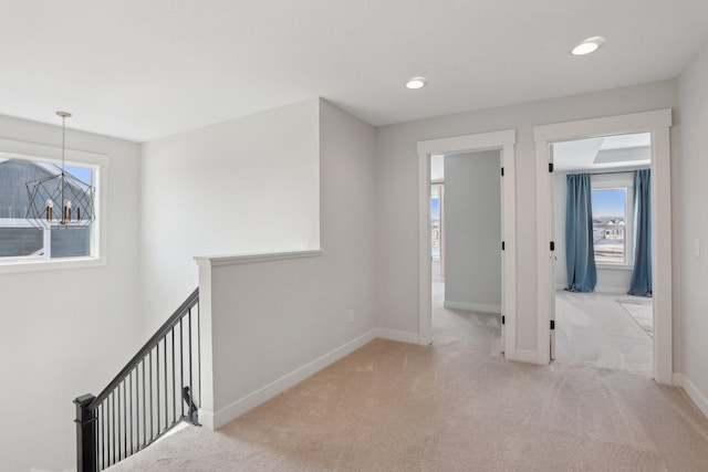 hall featuring light colored carpet, baseboards, a healthy amount of sunlight, and an upstairs landing