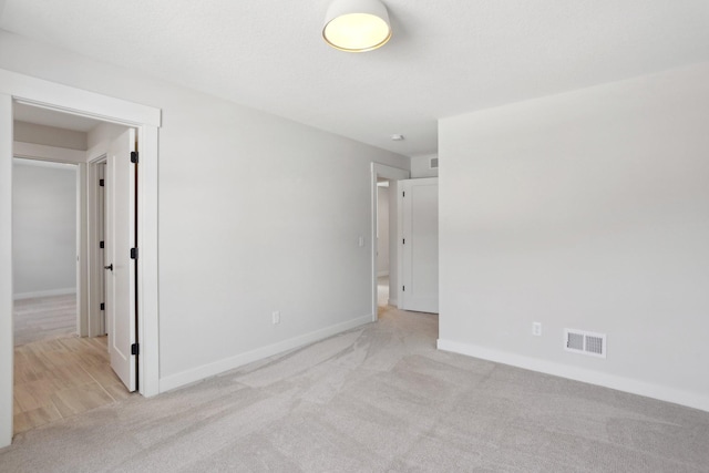 interior space with baseboards, visible vents, and light colored carpet