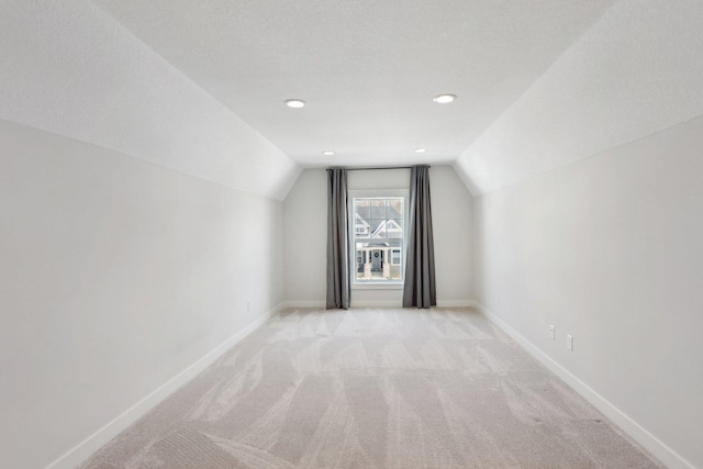 bonus room featuring lofted ceiling, a textured ceiling, light colored carpet, and baseboards