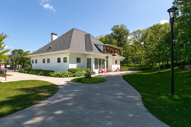 view of property exterior featuring a patio, a chimney, a shingled roof, a lawn, and fence