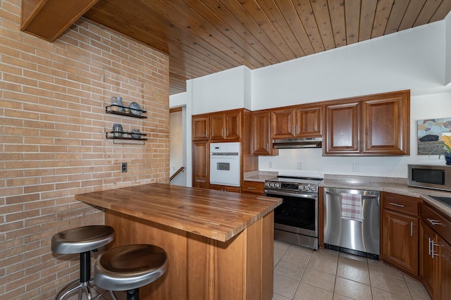 kitchen featuring wood ceiling, brick wall, appliances with stainless steel finishes, wooden counters, and light tile patterned flooring