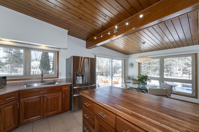 kitchen with light tile patterned floors, lofted ceiling with beams, a sink, wood counters, and stainless steel fridge