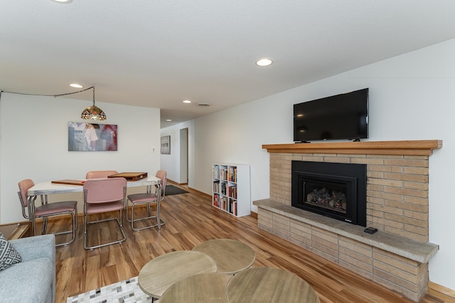 living area with recessed lighting, a brick fireplace, and wood finished floors