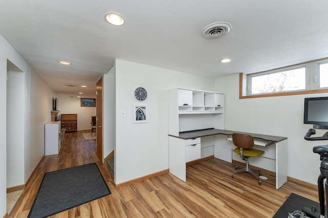 home office featuring light wood finished floors, baseboards, visible vents, a textured ceiling, and built in desk