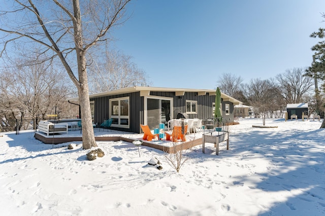 snow covered back of property with a deck, a storage shed, an outdoor structure, a sunroom, and board and batten siding