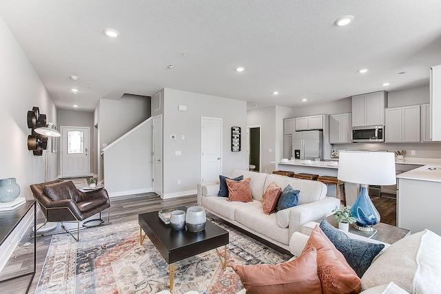 living area featuring a textured ceiling, recessed lighting, wood finished floors, baseboards, and stairway