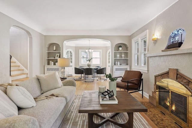 living room featuring built in shelves, a fireplace, wood finished floors, and baseboards