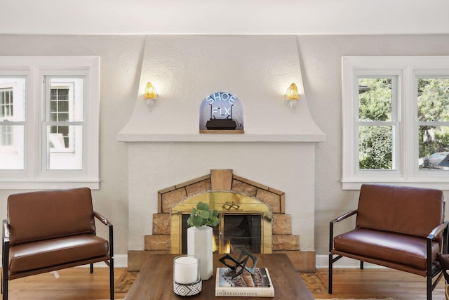 living area featuring a lit fireplace, baseboards, wood finished floors, and a textured wall