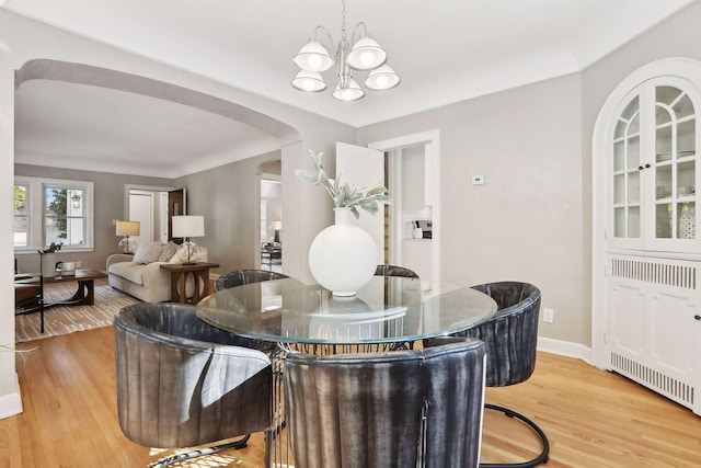 dining space featuring baseboards, arched walkways, a chandelier, and wood finished floors