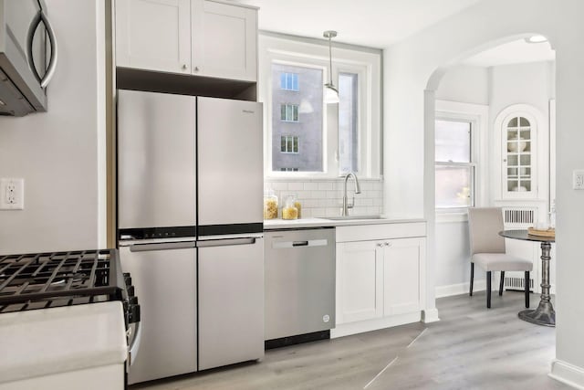 kitchen featuring white cabinets, appliances with stainless steel finishes, decorative light fixtures, light countertops, and a sink