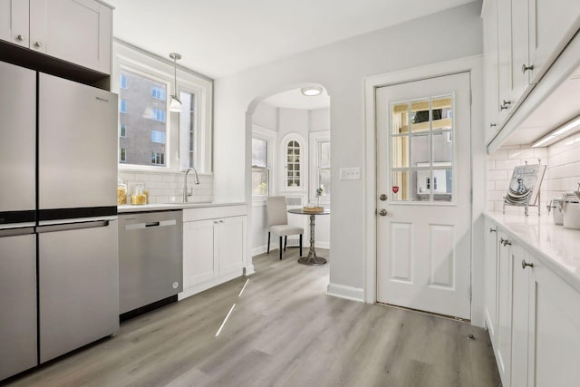 kitchen featuring arched walkways, appliances with stainless steel finishes, light countertops, white cabinetry, and pendant lighting