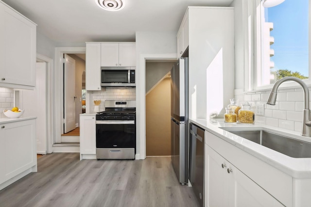 kitchen featuring light wood finished floors, white cabinets, appliances with stainless steel finishes, light countertops, and a sink