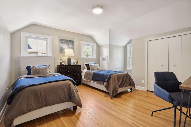 bedroom with light wood-type flooring, a closet, lofted ceiling, and baseboards