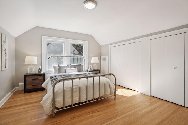 bedroom featuring light wood-type flooring, lofted ceiling, and two closets