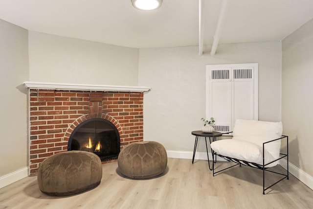 living area with beam ceiling, baseboards, a fireplace, and light wood finished floors