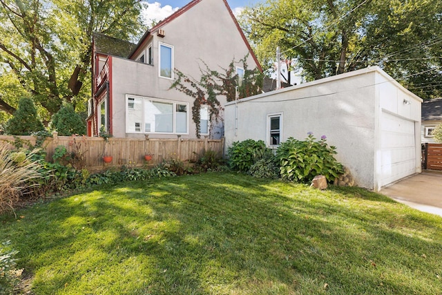 exterior space featuring a garage, a lawn, fence, and stucco siding