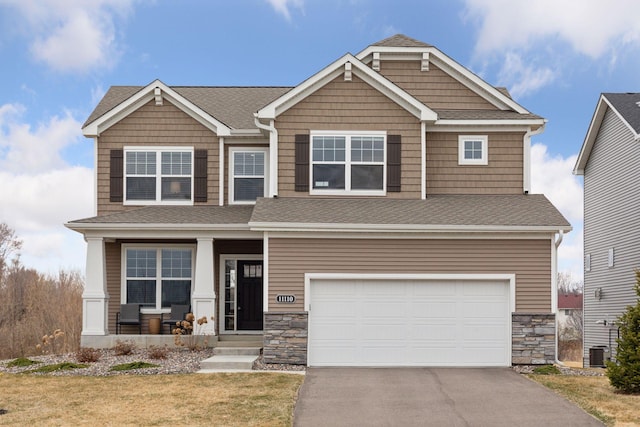 craftsman-style home featuring an attached garage, driveway, stone siding, and covered porch
