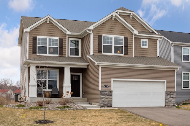 craftsman-style house with central air condition unit, driveway, a front yard, a garage, and covered porch