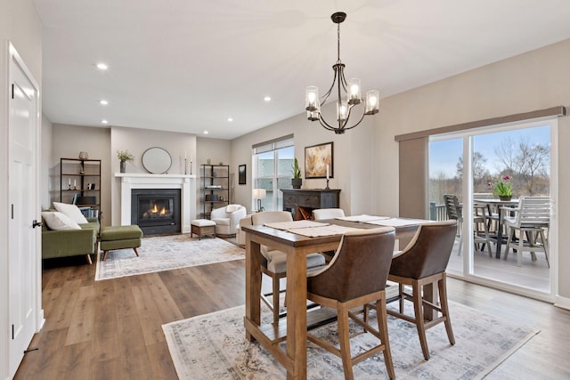 dining room with a glass covered fireplace, recessed lighting, an inviting chandelier, and wood finished floors