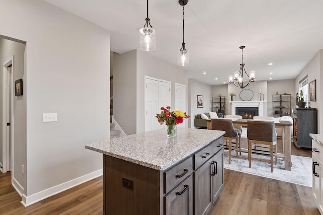 kitchen featuring baseboards, decorative light fixtures, dark wood-style flooring, a warm lit fireplace, and a kitchen island