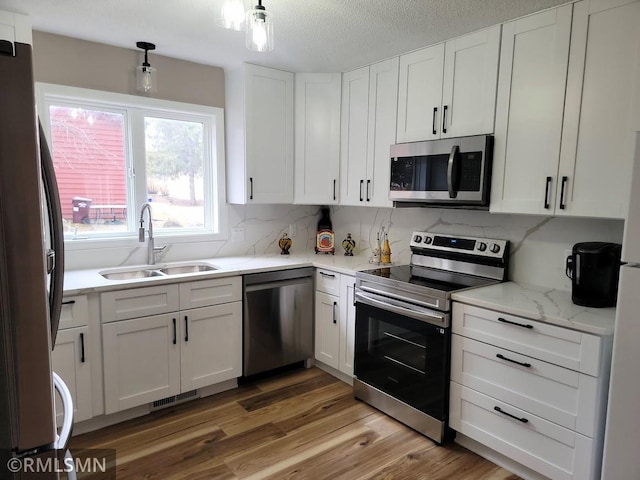 kitchen featuring a sink, light wood-style floors, white cabinets, appliances with stainless steel finishes, and decorative backsplash