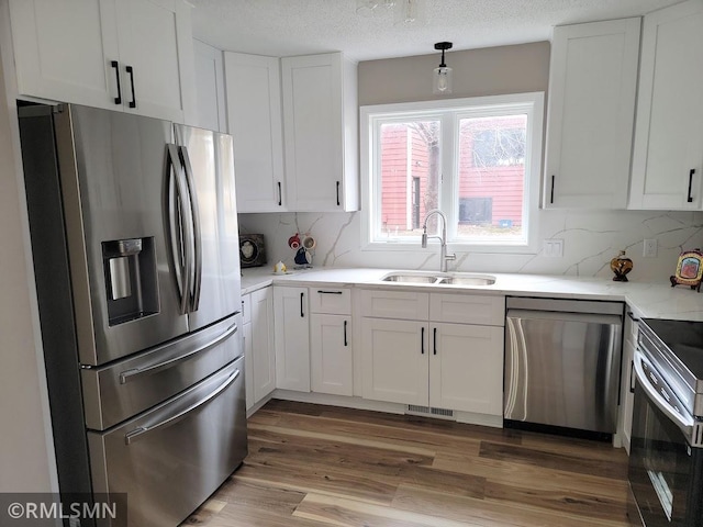 kitchen featuring a sink, white cabinets, appliances with stainless steel finishes, light wood finished floors, and tasteful backsplash